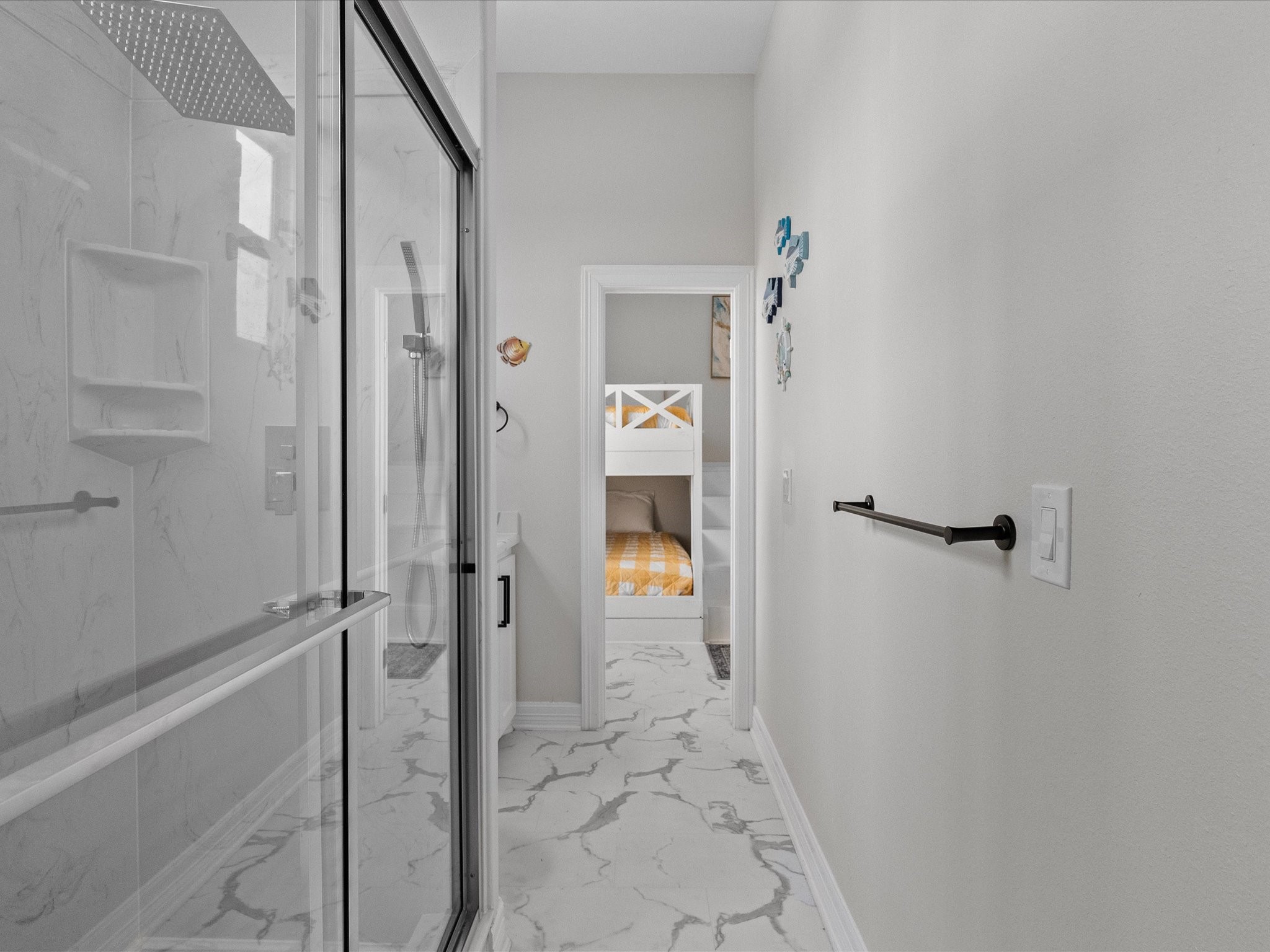 1018 Seashell Drive Surfside Beach, TX 77541 - Photo 27 of 49 This photo features a bright, modern bathroom with a glass-enclosed shower and marble-patterned flooring. The hallway leads to a cozy bedroom with bunk beds, perfect for a family.