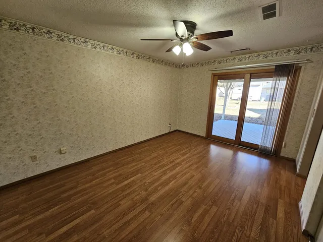 an empty room with wooden floor fan and windows