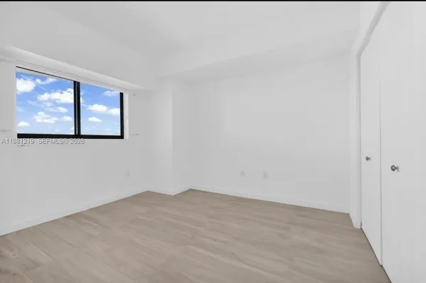 a view of an empty room with wooden floor and a window