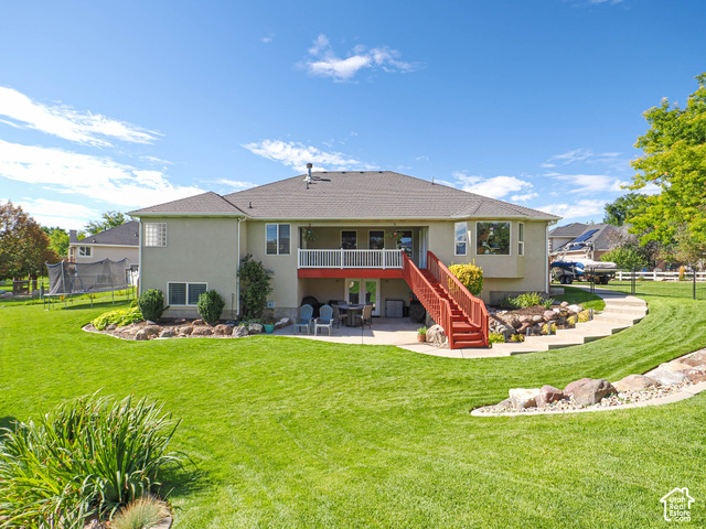 11779 South Stone Ridge Court Ridge West Riverton, UT 84065 - Photo 71 of 85 Expansive green lawn with established landscaping beds, a multi-level deck with white railings, and a lower-level patio