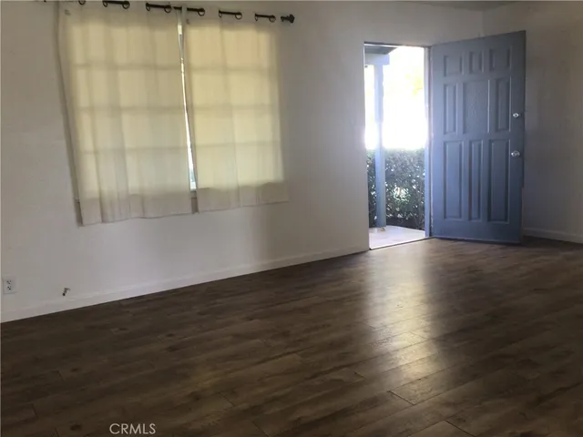 an empty room with wooden floor and windows with curtains