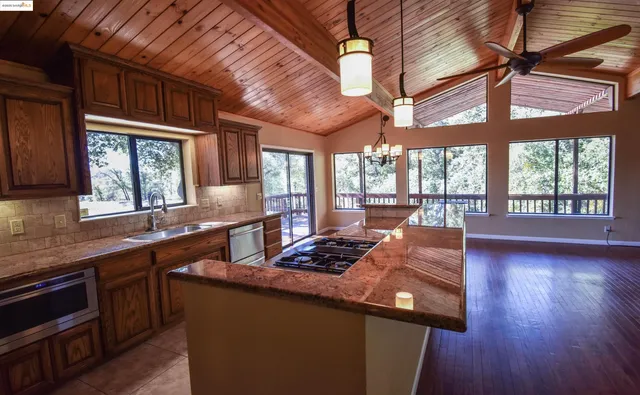 a kitchen with stainless steel appliances granite countertop wooden cabinets a stove a sink and a large window