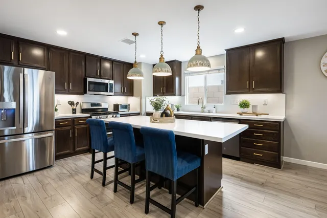 a kitchen with stainless steel appliances granite countertop a sink a stove a refrigerator and island with wooden floor