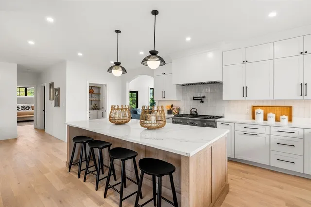 a kitchen with kitchen island granite countertop a stove a sink a refrigerator and white cabinets with wooden floor