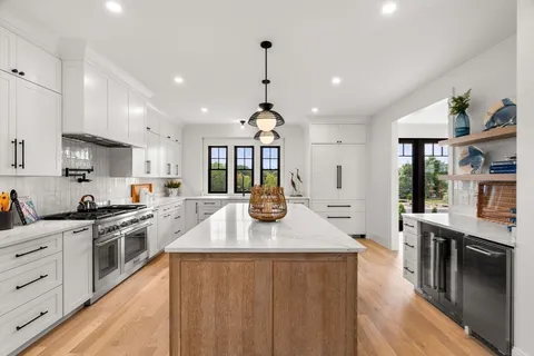 a kitchen with kitchen island granite countertop a stove a sink a refrigerator and white cabinets with wooden floor