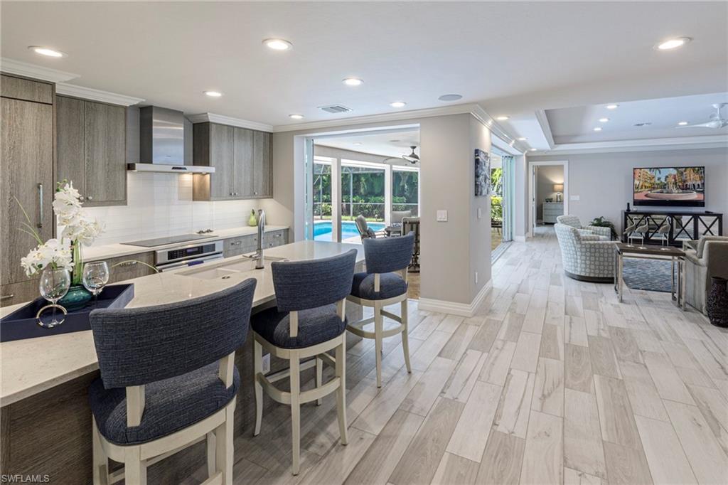 3720 Parkview Way Naples, FL 34103 - Photo 12 of 29 Kitchen featuring ceiling fan, light hardwood / wood-style floors, tasteful backsplash, a raised ceiling, and wall chimney exhaust hood