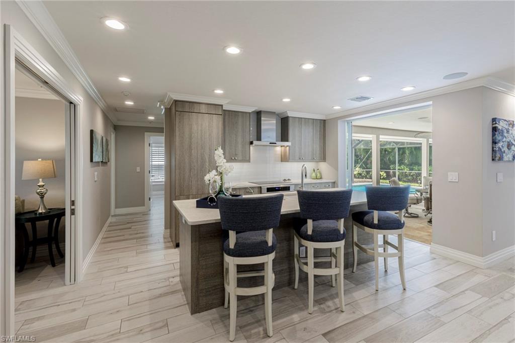 3720 Parkview Way Naples, FL 34103 - Photo 18 of 29 Kitchen with wall chimney range hood, tasteful backsplash, ornamental molding, light wood-type flooring, and a breakfast bar