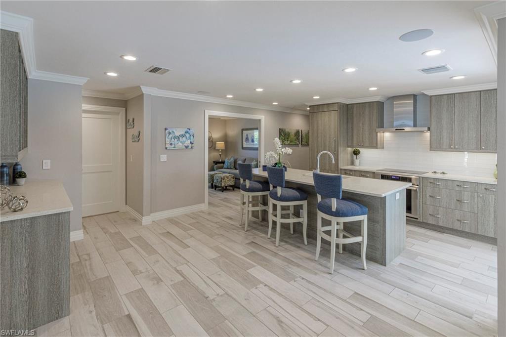 3720 Parkview Way Naples, FL 34103 - Photo 5 of 29 Kitchen featuring light hardwood / wood-style floors, a kitchen breakfast bar, tasteful backsplash, an island with sink, and wall chimney exhaust hood