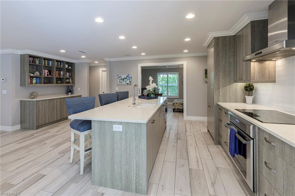 3720 Parkview Way Naples, FL 34103 - Photo 10 of 29 Kitchen with an island with sink, black electric cooktop, wall chimney exhaust hood, oven, and sink