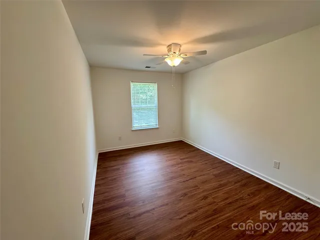an empty room with wooden floor chandelier fan and windows