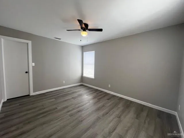 an empty room with wooden floor ceiling fan and windows