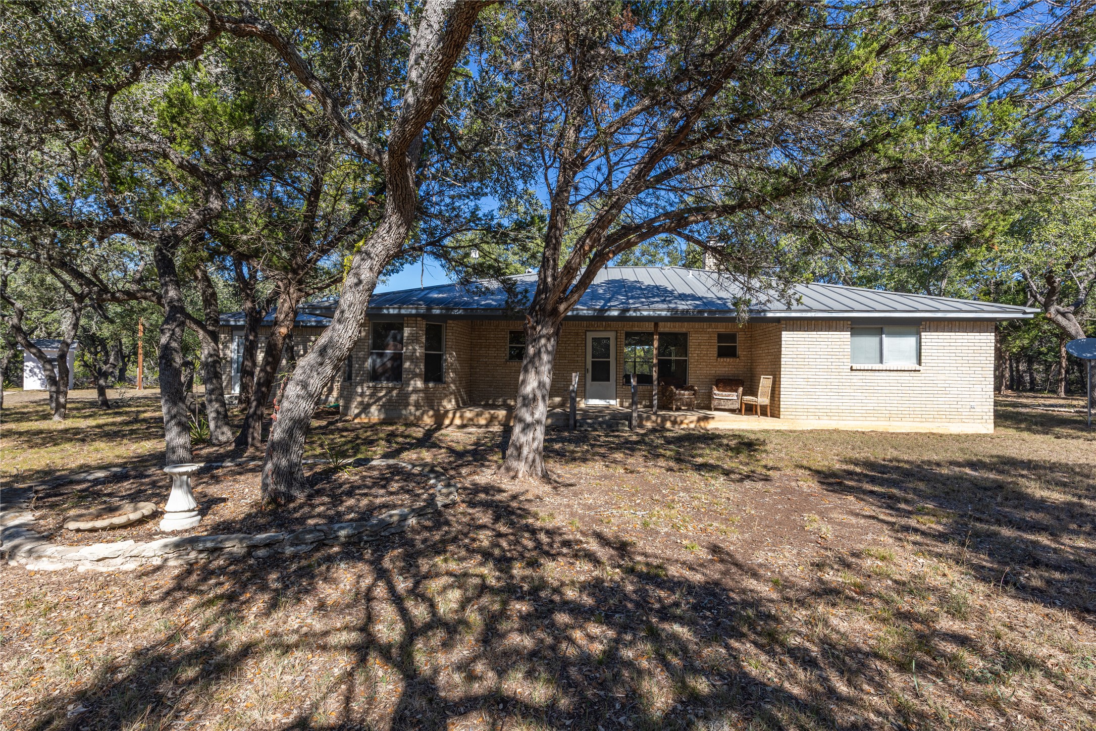 2501 Fischer Store Road Wimberley, TX 78676 - Photo 20 of 23 Rear exterior featuring light-colored brick siding, a metal roof, and a concrete patio