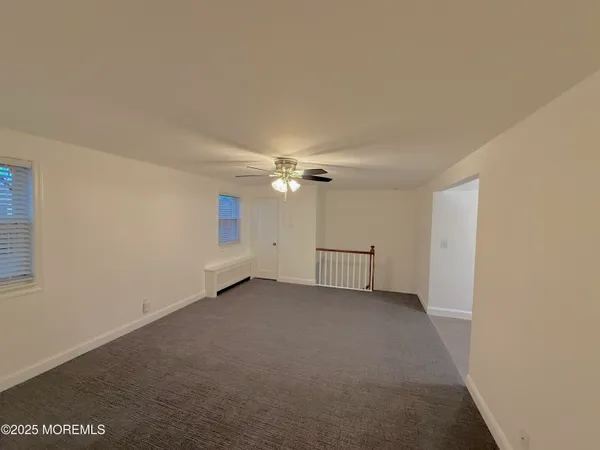 an empty room with chandelier fan and windows