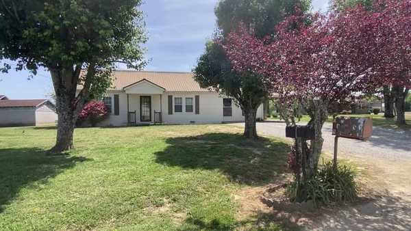 a front view of a house with a yard and large tree