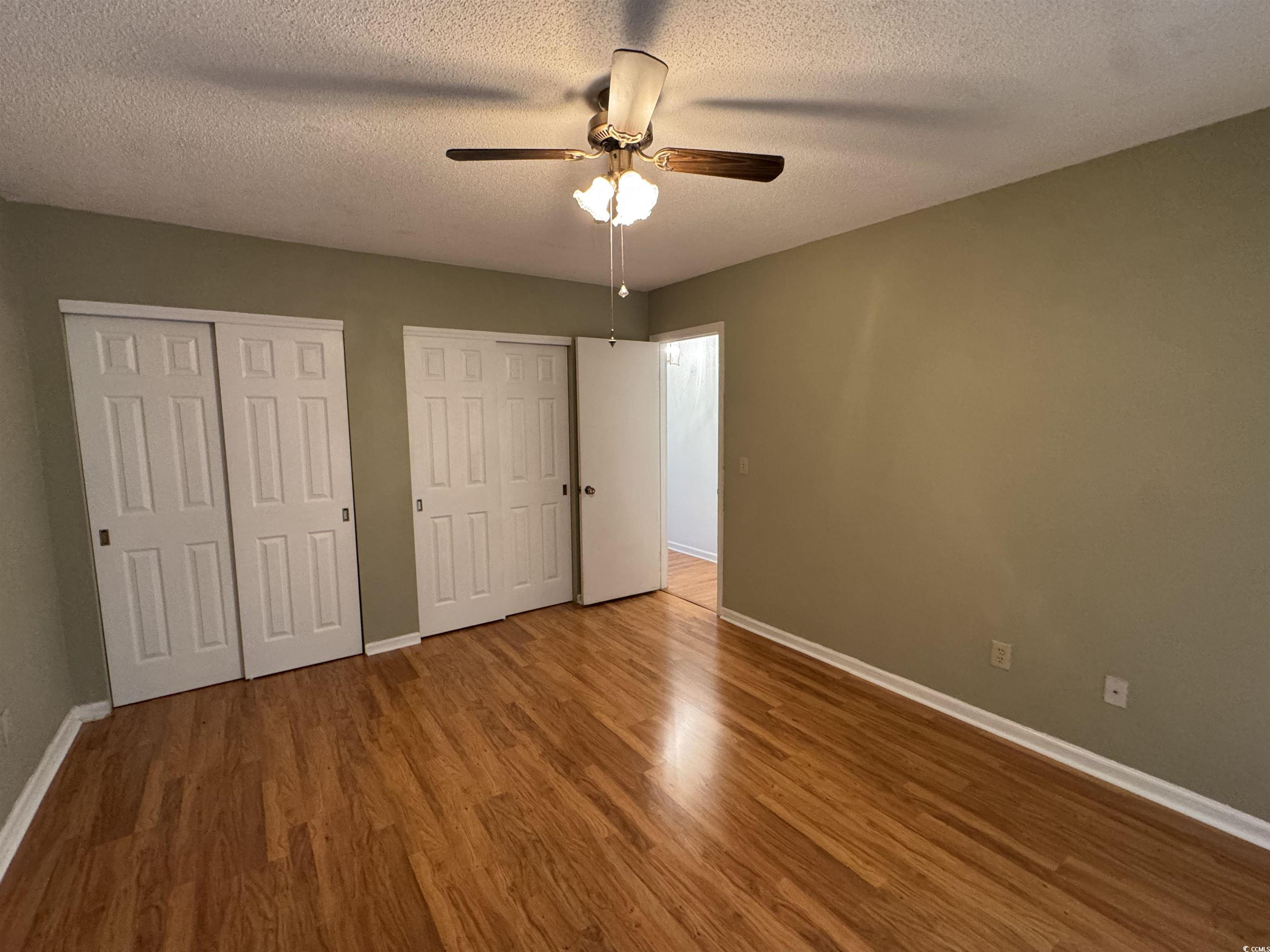 58 Wedgefield Village Road, Unit 48 Georgetown, SC 29440 - Photo 20 of 23 Unfurnished bedroom featuring two closets, a textured ceiling, ceiling fan, and wood finished floors