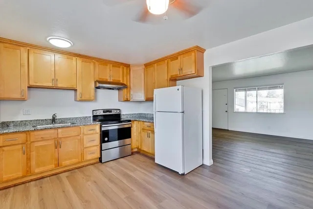 a kitchen with granite countertop a refrigerator a stove a sink cabinets and wooden floor