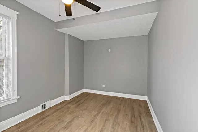an empty room with wooden floor fan and windows