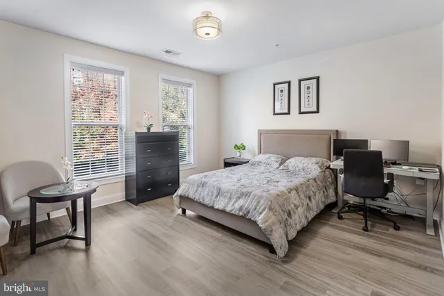 a bedroom with a bed a desk and chair with wooden floor