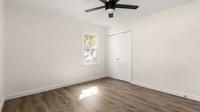 an empty room with wooden floor ceiling fan and windows