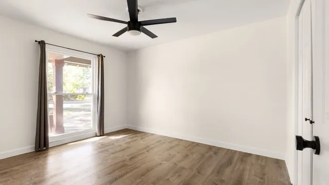 an empty room with wooden floor fan and windows