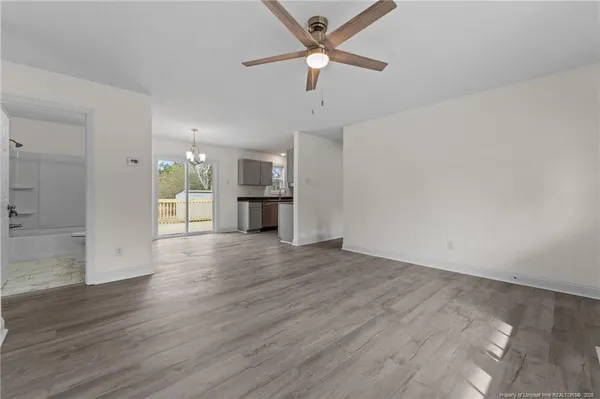 an empty room with wooden floor chandelier fan and windows