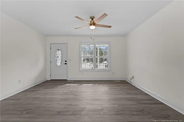 an empty room with wooden floor chandelier fan and windows