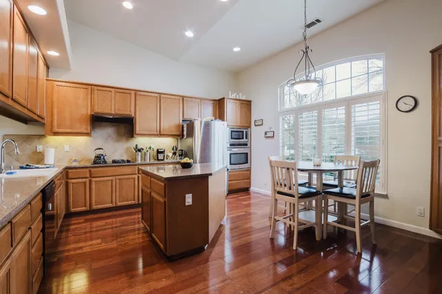 a kitchen with stainless steel appliances granite countertop a stove refrigerator and a dining table with wooden floor