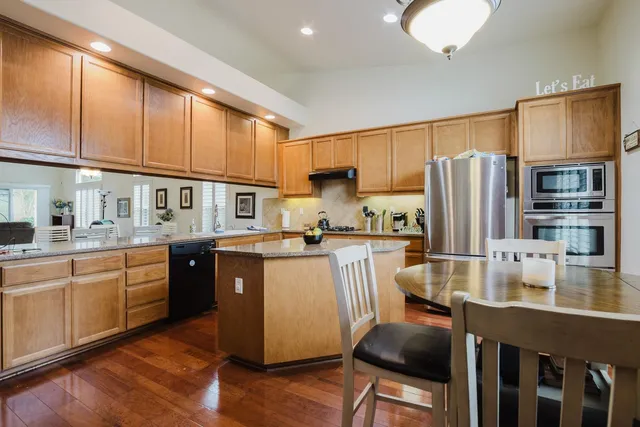 a kitchen with stainless steel appliances granite countertop a refrigerator a stove top oven a sink dishwasher and wooden cabinets with wooden floor