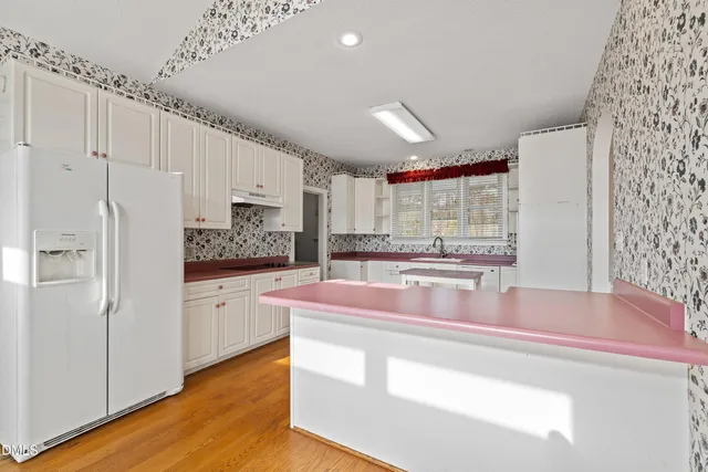 a kitchen with stainless steel appliances granite countertop a refrigerator a sink and white cabinets with wooden floor