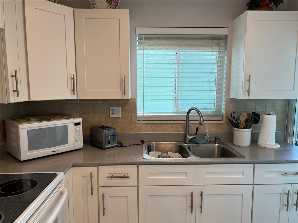 2100 Northeast 38th Street, Unit 124 Lighthouse Point, FL 33064 - Photo 3 of 30 a kitchen with white cabinets a sink and a stove with wooden floor