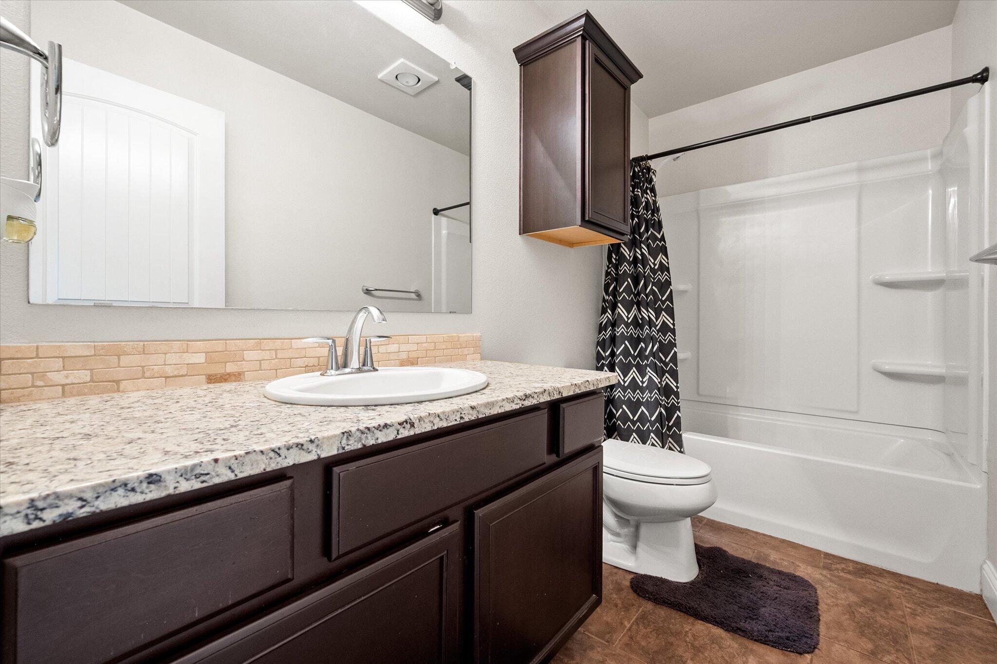 7026 97th Street Lubbock, TX 79424 - Photo 19 of 30 a bathroom with a granite countertop sink a toilet a mirror and shower