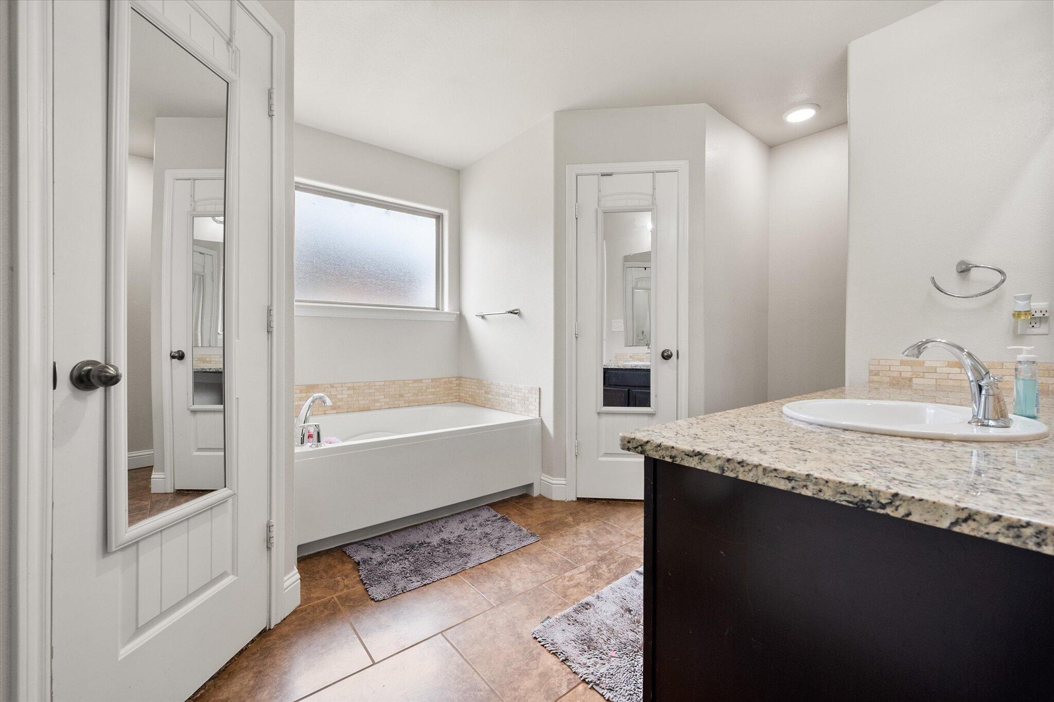 7026 97th Street Lubbock, TX 79424 - Photo 23 of 30 a bathroom with a granite countertop sink a mirror and a bathtub