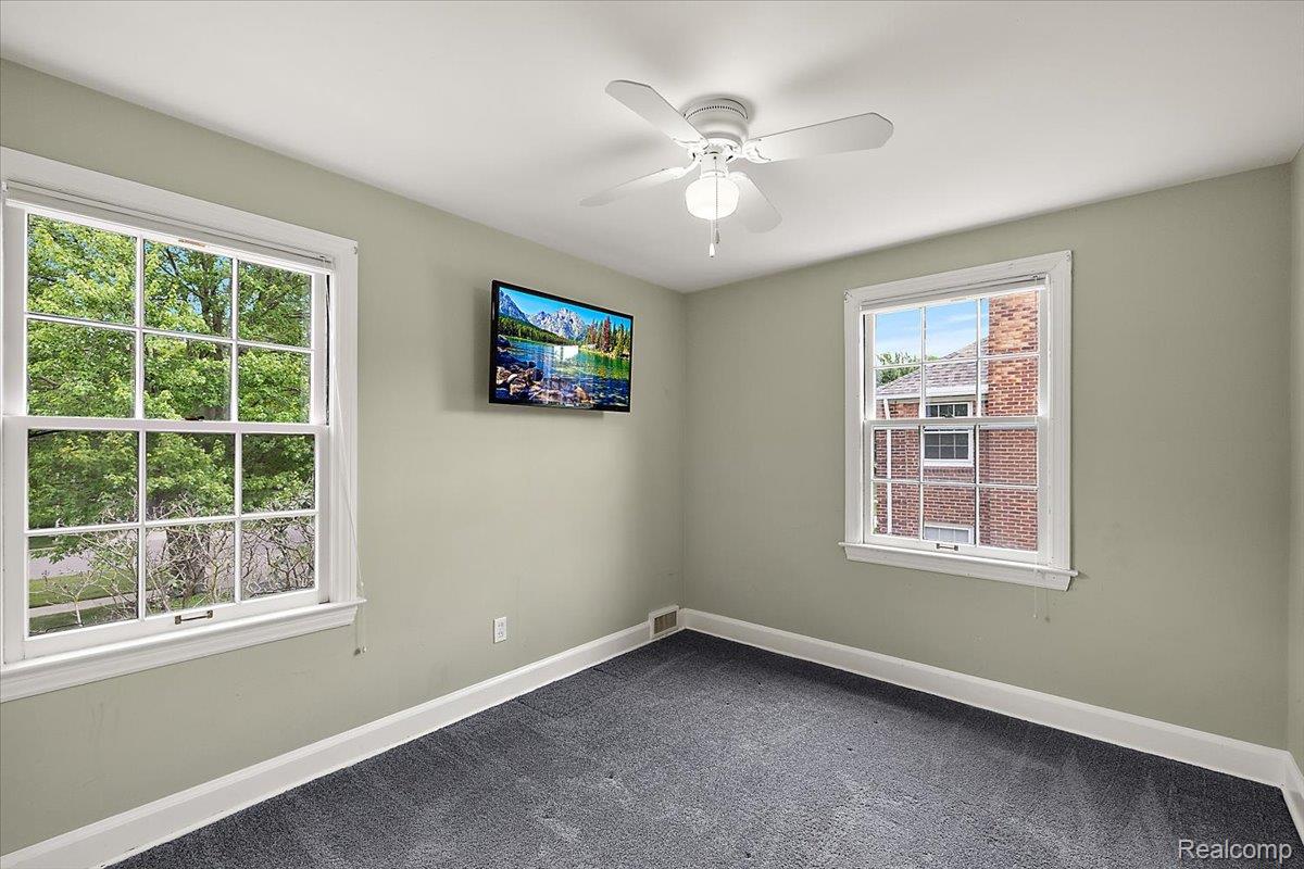 1051 Devonshire Road Grosse Pointe, MI 48230 - Photo 39 of 99 Room featuring two double-hung windows with white trim, a white ceiling fan with light fixture, light gray wall paint, and dark gray carpet flooring