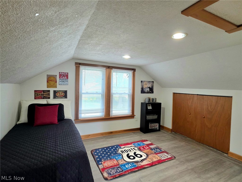 2335 West River Road Newton Falls, OH 44444 - Photo 22 of 36 Attic space featuring pitched ceilings, recessed lighting, double windows with wood trim, wood-finish flooring, and a built-in closet with wood bi-fold doors