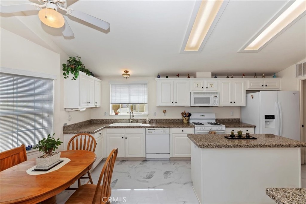 27250 Murrieta Road, Unit 298 Menifee, CA 92586 - Photo 17 of 54 a kitchen with granite countertop a sink white cabinets a stove a dining table and chairs