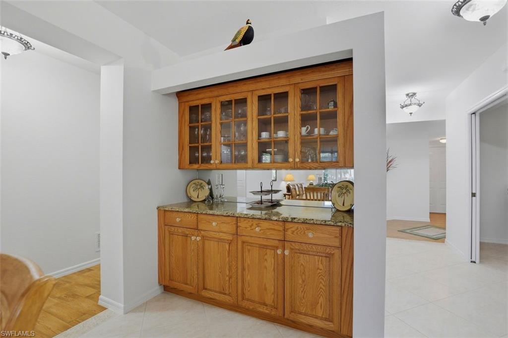 23820 San Marino Road, Unit 102 Estero, FL 34135 - Photo 13 of 28 Bar area with light stone countertops, wood finish cabinets, glass insert cabinets, and light tile patterned floors