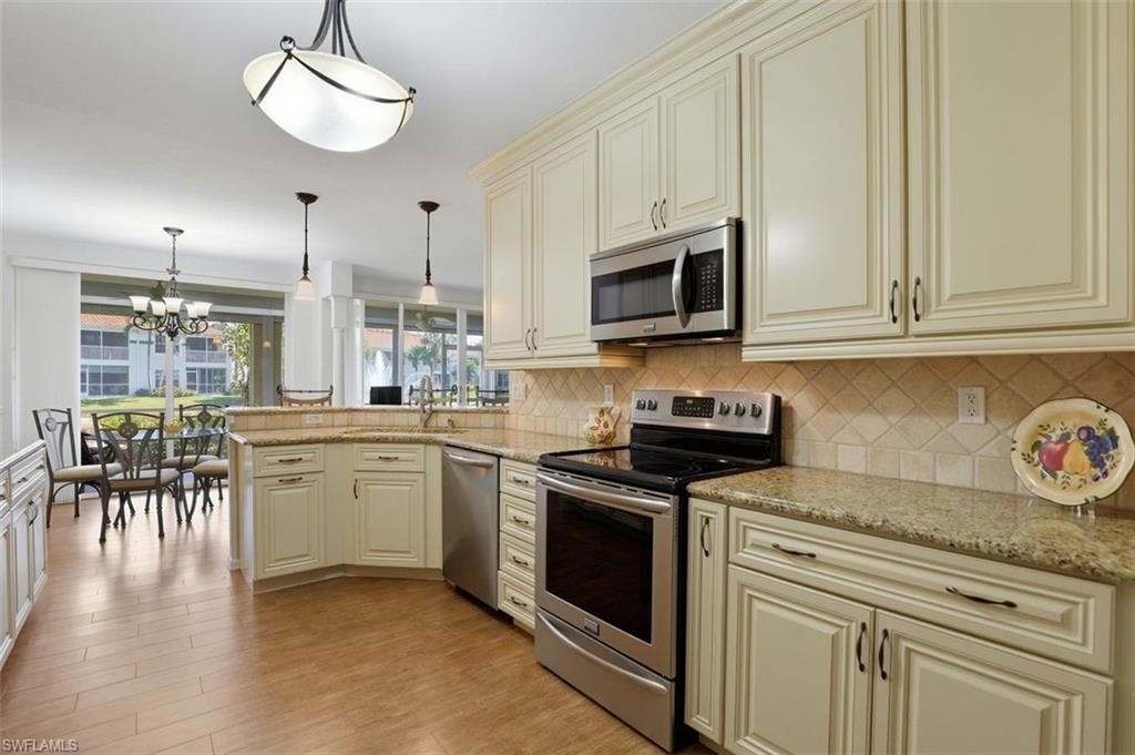 23820 San Marino Road, Unit 102 Estero, FL 34135 - Photo 7 of 28 Kitchen with cream cabinets, stainless steel appliances, a peninsula, and light stone countertops