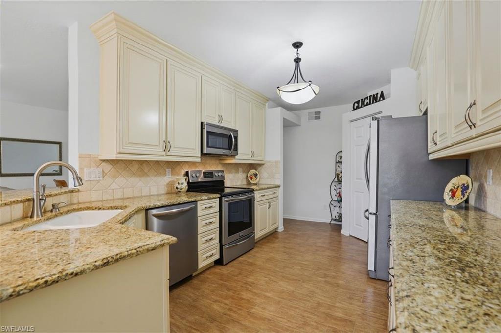 23820 San Marino Road, Unit 102 Estero, FL 34135 - Photo 8 of 28 Kitchen with stainless steel appliances, light stone counters, hanging light fixtures, and light wood-style floors