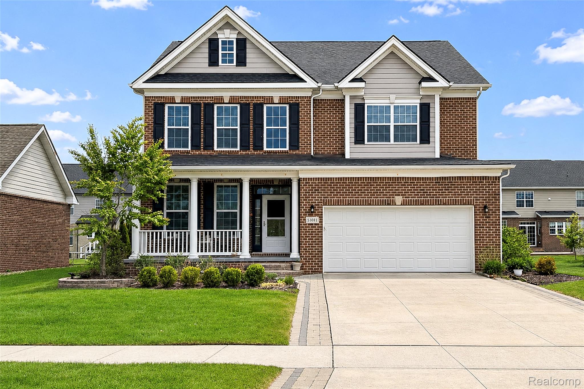 Traditional home featuring covered porch, concrete driveway, a garage, and brick siding