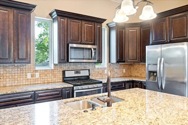a kitchen with stainless steel appliances granite countertop a refrigerator a stove a sink and a wooden cabinets