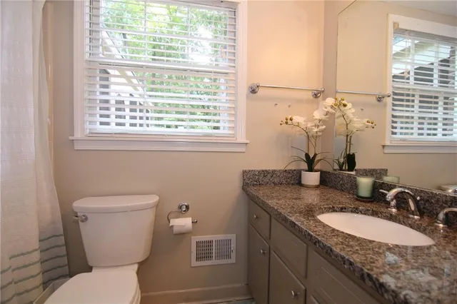 a bathroom with a granite countertop toilet a sink and a window