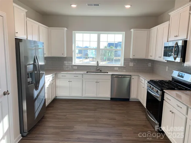 a kitchen with a white cabinets a sink a window a wooden floor and stainless steel appliances