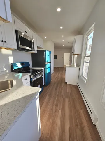 a kitchen with stainless steel appliances a microwave a stove a sink a refrigerator white cabinets and wooden floor