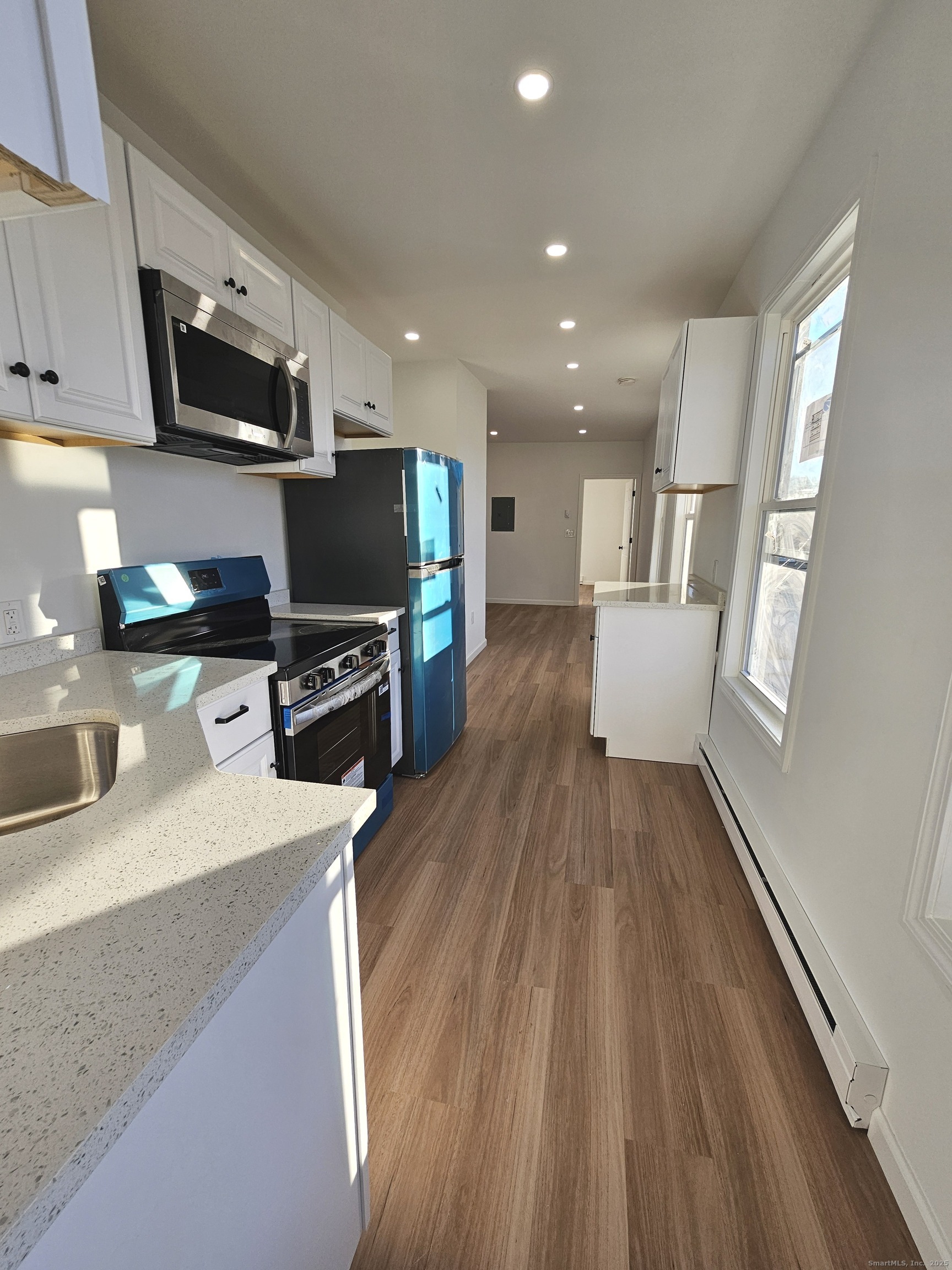 a kitchen with stainless steel appliances a microwave a stove a sink a refrigerator white cabinets and wooden floor