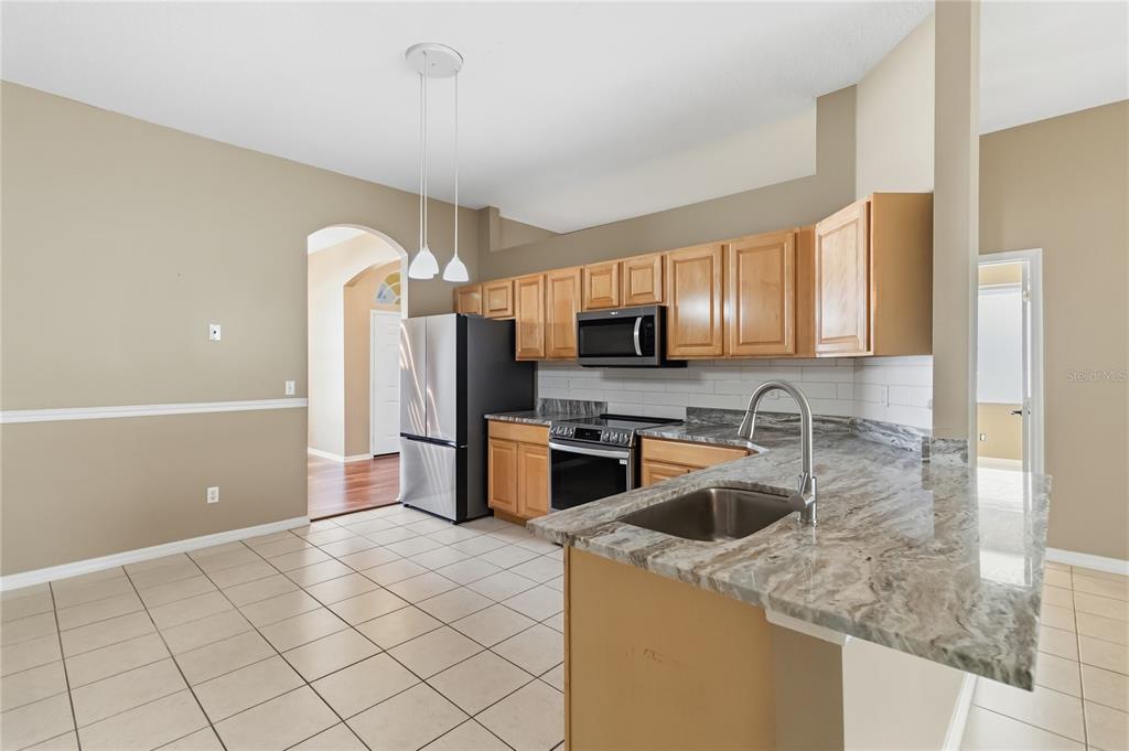 677 Buckhaven Loop Ocoee, FL 34761 - Photo 9 of 41 a kitchen with stainless steel appliances granite countertop a sink a stove a refrigerator a washer dryer and white cabinets