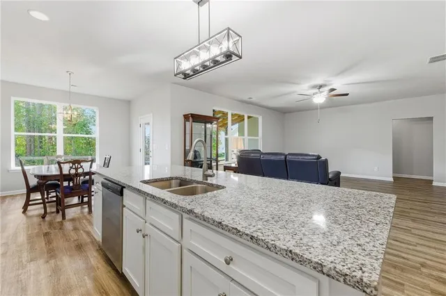 a kitchen with granite countertop a stove a sink a dining table and chairs with wooden floor