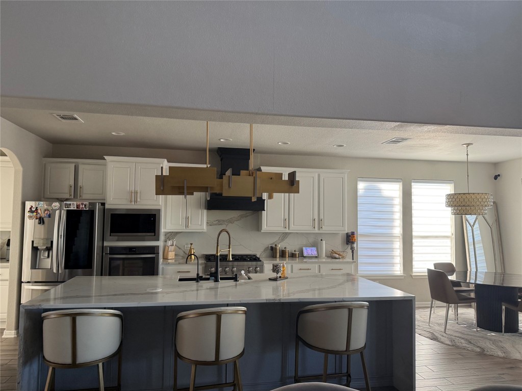 Undisclosed Address Leander, TX 78641 - Photo 6 of 8 Kitchen featuring stainless steel appliances, a breakfast bar, light stone counters, white cabinetry, and an island with sink