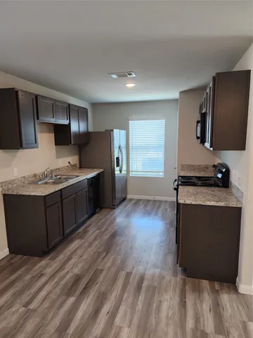 a kitchen with stainless steel appliances granite countertop a stove a sink dishwasher and a refrigerator with wooden floor