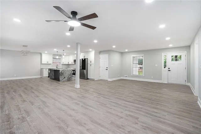 an empty room with wooden floor a ceiling fan and kitchen view