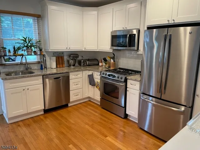 a kitchen with white cabinets stainless steel appliances and wooden floor